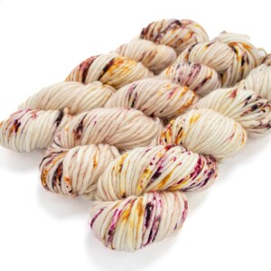 May include: A skein of cream-coloured yarn with flecks of purple, orange, and brown.
