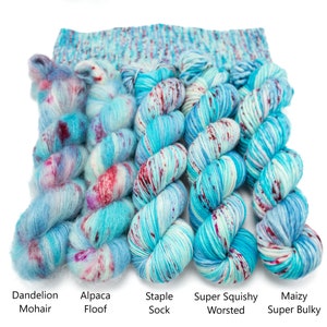 May include: Five skeins of yarn in different weights, from left to right: Dandelion Mohair, Alpaca Floof, Staple Sock, Super Squishy Worsted, and Maizy Super Bulky. The yarn is a mix of blue, white, and red.