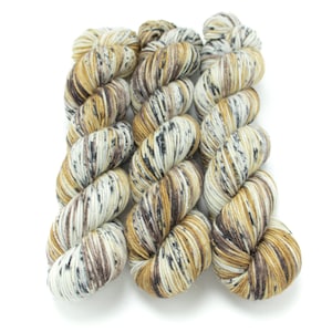 May include: Three skeins of yarn in a speckled pattern of brown, beige, and white with black flecks.