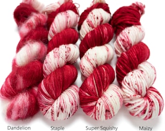 May include: Four skeins of yarn in different weights, from left to right: Dandelion Mohair, Staple Sock, Super Squishy Worsted, and Maizy Super Bulky. All skeins are a red and white colorway with a speckled pattern.