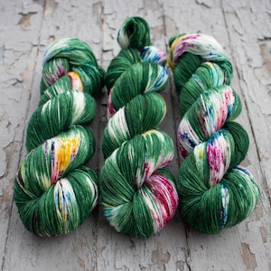 May include: Three skeins of yarn in green, white, and pink with a floral pattern. The yarn is wound into a ball shape.