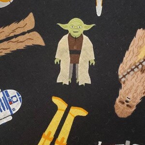 May include: A black fabric with a repeating pattern of Star Wars characters. The characters include Yoda, Chewbacca, C-3PO, R2-D2, and X-Wing fighters.