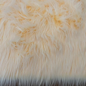 Pode incluir: Close-up de um tecido de pele sintética macio, felpudo e de cor creme. O tecido tem uma pilha longa e uma superfície ligeiramente texturizada.