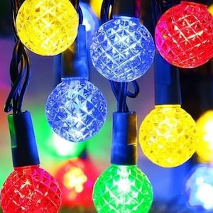 May include: A string of colorful globe-shaped LED lights. The lights are in various colors, including red, yellow, blue, and green. The bulbs have a textured, diamond-like pattern. The string is on a black wire, and the background is blurred.