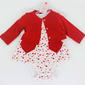 May include: A red cardigan with a white bodysuit and a white dress with a heart pattern. The dress has red heart accents. The tag says "Just One You Carter's".
