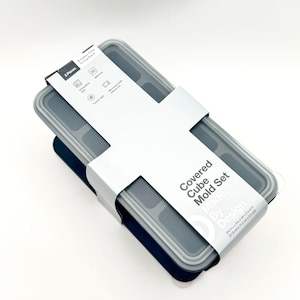 May include: A dark gray silicone covered cube mold set with a white paper sleeve. The sleeve text reads Covered Cube Mold Set Made By Design, 8 cubes total, 1/2 cup each, and dimensions of 8 5/8 in L x 4 3/8 in W x 2 1/16 in H.