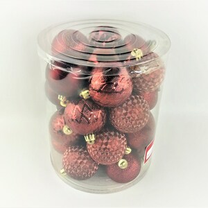 Op de afbeelding: Een doorzichtige plastic container gevuld met rode kerstballen. De ballen hebben een glanzende, textuur.