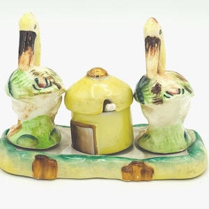 May include: A vintage ceramic salt and pepper shaker set with a matching sugar bowl. The set features a whimsical design of bird-like figures with yellow beaks and green accents. The tray is painted with green and brown details.