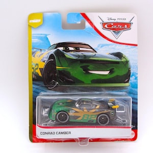 May include: A green and gold toy race car named Conrad Camber, packaged on a Disney Pixar Cars card. The car has the number 82 on the side and is in a clear plastic case. The card features a larger image of the car.