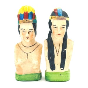 Può includere: Due statuette vintage in ceramica raffiguranti figure native americane. Una indossa un copricapo colorato, l'altra ha lunghi capelli neri. Entrambe hanno tratti del viso dipinti e basi verdi. Le statuette sono probabilmente della metà del XX secolo.