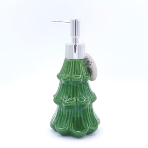 May include: Green ceramic soap dispenser in the shape of a Christmas tree. The dispenser has a silver-colored pump and a tag attached. The tree-shaped body has a glossy finish and detailed texture.
