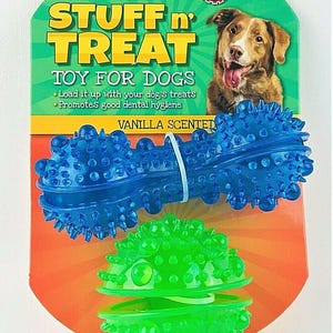 May include: A two-piece dog toy set. The packaging features a green and orange background with the words "STUFF n' TREAT" and "TOY FOR DOGS". The set includes a blue bone-shaped toy and a green ball-shaped toy. The toys are vanilla scented.