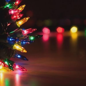 May include: Close-up of a string of Christmas lights with various colored bulbs, including red, green, yellow, and blue. The lights are on a dark background, creating a festive and warm atmosphere. Perfect for holiday decorations.