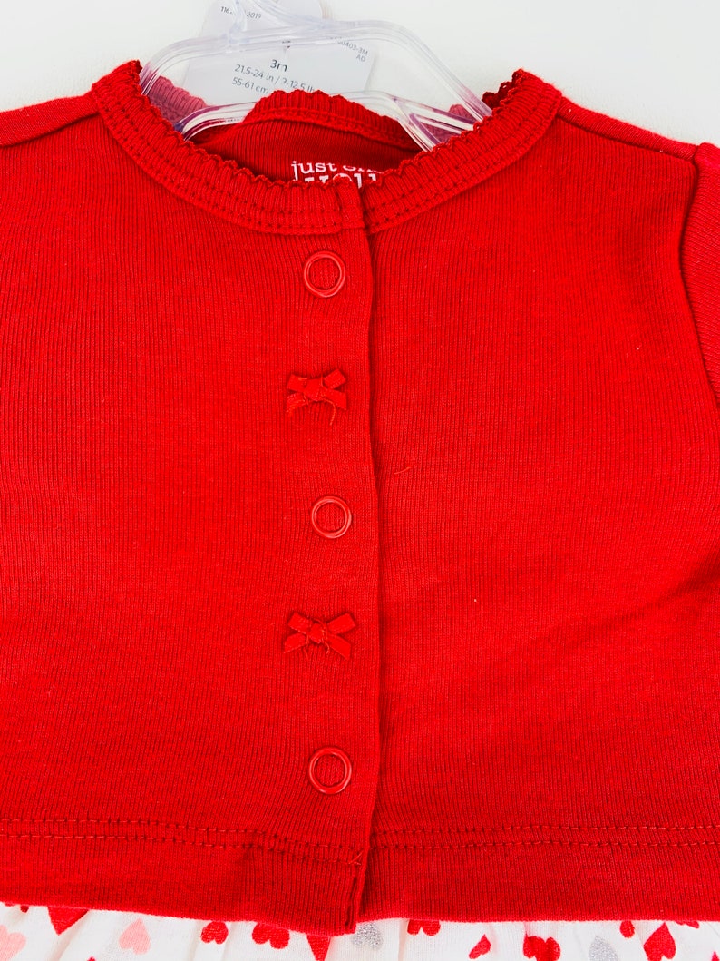 May include: Red ribbed cardigan with a white and pink heart print skirt. The cardigan has a scalloped neckline and four buttons with bows. The text "Just One You" is visible on the tag.