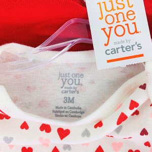 May include: A two-piece baby outfit with a red long-sleeve shirt and a white long-sleeve shirt with a heart print. The white shirt has the text "just one you made by carter's" and "3M" printed on the tag.