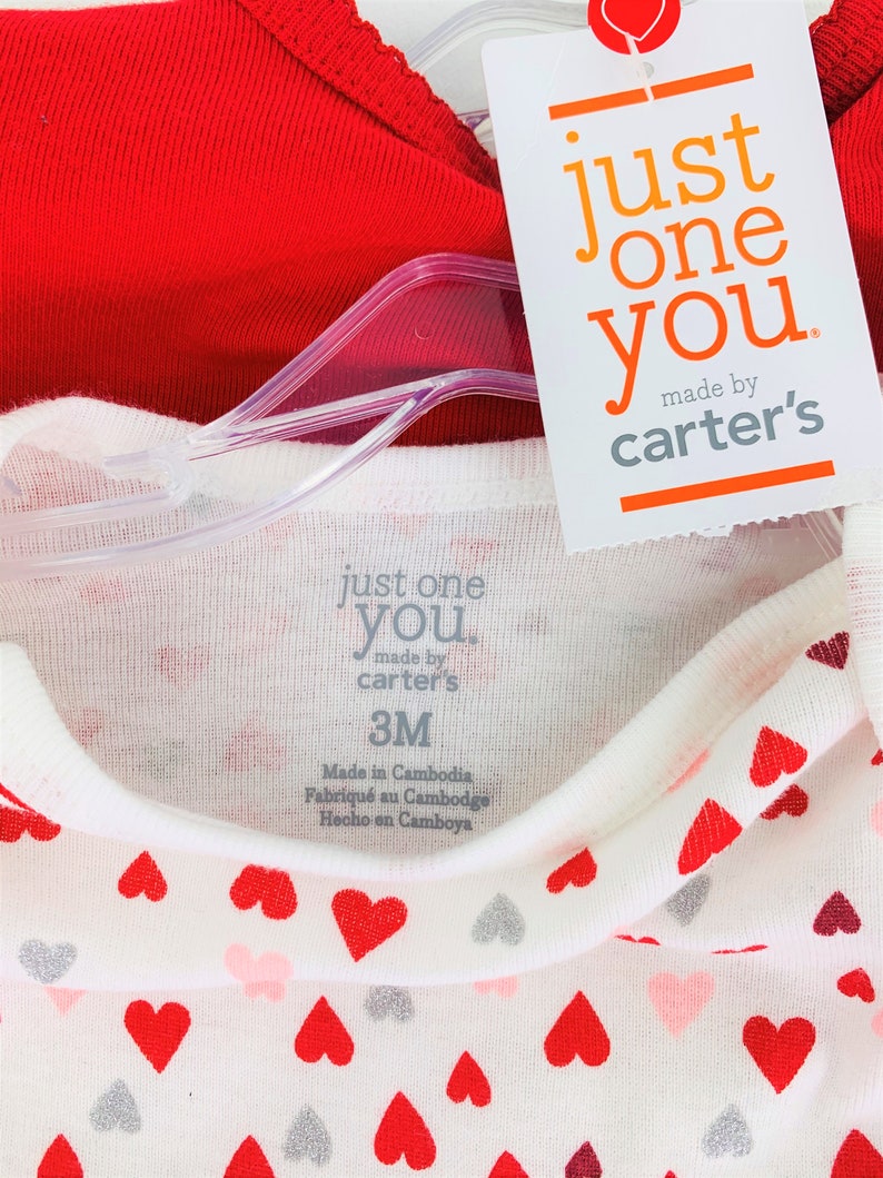 May include: A two-piece baby outfit with a red long-sleeve shirt and a white long-sleeve shirt with a heart print. The white shirt has the text "just one you made by carter's" and "3M" printed on the tag.