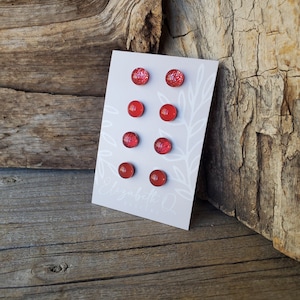 May include: A set of six red glitter stud earrings displayed on a white card with the text "Elizabeth Q Jewelry".