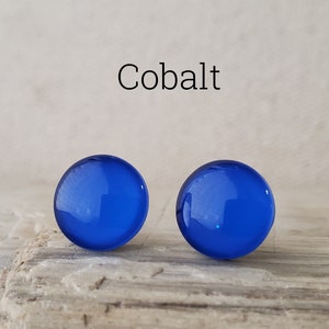May include: A pair of round, smooth, cobalt blue stud earrings with a glossy finish. The word Cobalt is printed in black text above the earrings, which feature a vibrant, solid blue color and a simple, circular shape with a reflective surface.