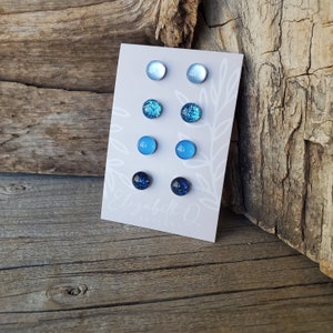 May include: A set of six blue and white stud earrings on a white card with the text "Elizabeth Q Designs". The earrings are arranged in a gradient from light blue to dark blue.