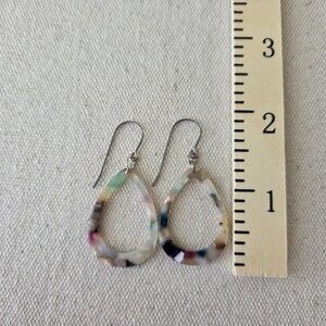 May include: A pair of teardrop earrings with a colorful, marbled pattern. The earrings are approximately 1.5 inches long and feature a silver-tone hook. The colors include white, pink, green, and black.