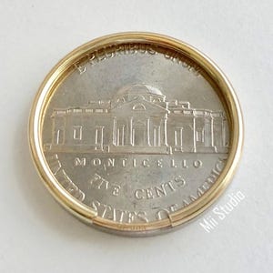 May include: A gold-plated US nickel coin with the image of Monticello on the front. The coin is surrounded by a gold band.