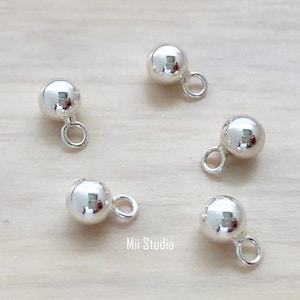 May include: Four silver ball charms with a small loop for attaching to jewelry or other crafts. The charms are smooth and shiny.
