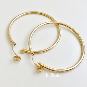 May include: A pair of gold hoop earrings with a simple, classic design. The earrings are large and have a smooth, polished finish.