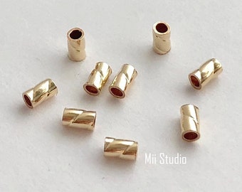 May include: Nine gold-colored metal beads with a twisted design. The beads are scattered on a white surface.