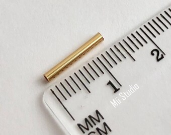 May include: A gold-colored metal tube measuring approximately 1 cm in length. The tube is placed on a ruler with millimeter and centimeter markings.