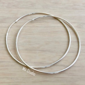 May include: A pair of large, silver hoop earrings. The hoops are thick and have a smooth, polished finish.
