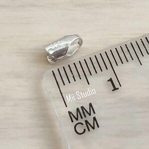 May include: A silver-toned metal clasp with a 925 stamp, measured against a ruler with markings in millimeters and centimeters.