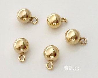 May include: Five gold-colored metal ball charms with a loop for attaching to jewelry or other crafts. The charms are round and have a smooth, shiny finish.