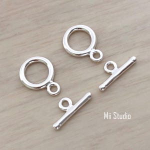 May include: Two silver toggle clasps with a round loop and a straight bar. The clasps are commonly used for jewelry making.