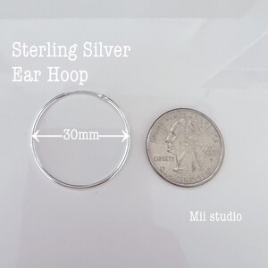 May include: Sterling silver ear hoop measuring 30mm in diameter. The hoop is shown next to a US quarter for size comparison.