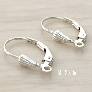 Puede incluir: Primer plano de dos cierres de pendientes de palanca plateados. Cada cierre tiene un lazo de alambre curvado, una palanca con bisagras y un extremo cónico decorativo. Los cierres están diseñados para la fabricación de joyas.