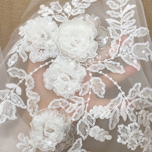 Puede incluir: Tela de encaje floral blanca con adornos de flores en 3D y lentejuelas. La tela tiene una textura delicada y transparente, ideal para añadir un toque de elegancia a cualquier proyecto.