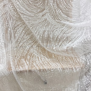 Peut inclure: Tissu de dentelle blanche perl&eacute;e avec un motif d&eacute;licat et tourbillonnant. Le tissu est transparent et a une texture douce et fluide.