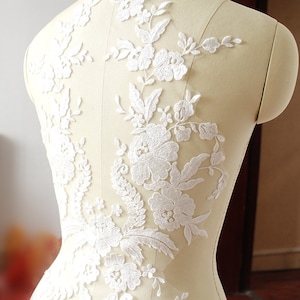 Op de afbeelding: Witte bloemenkant applique met delicate bloemen en bladeren. Deze kant applique is perfect om een ​​toets van elegantie toe te voegen aan elk kledingstuk.