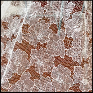 May include: White lace fabric with a floral pattern. The lace is delicate and intricate, with a repeating design of flowers and leaves.