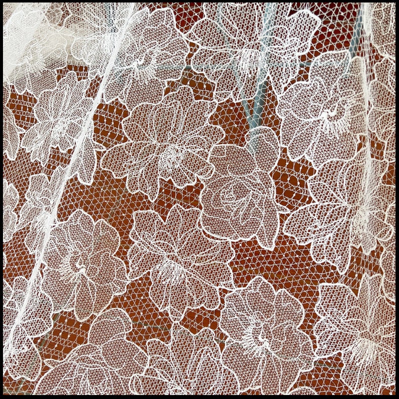May include: White lace fabric with a floral pattern. The lace is delicate and intricate, with a repeating design of flowers and leaves.