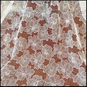 May include: White lace fabric with a floral pattern. The lace is delicate and intricate, with a fine mesh background.