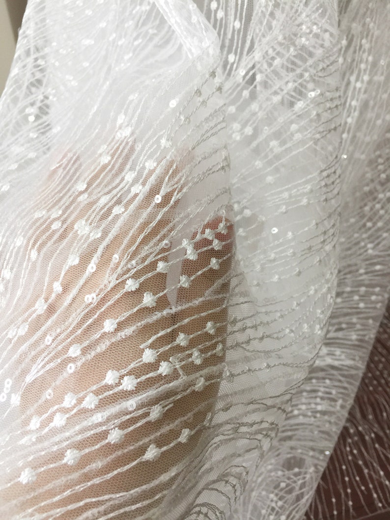 Peut inclure: Tissu blanc transparent avec un motif d&eacute;licat de petits points blancs. Le tissu a une texture douce et fluide.