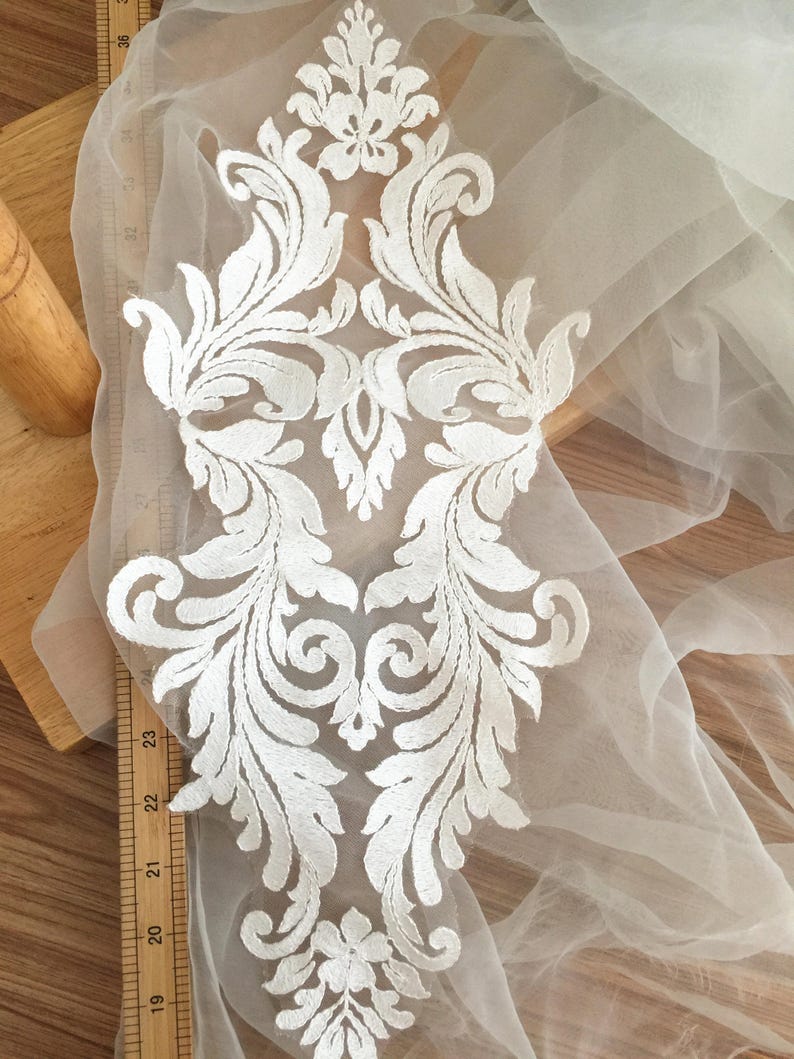 Puede incluir: Aplique de encaje blanco con un dise&ntilde;o floral. El aplique est&aacute; sobre una tela blanca transparente.