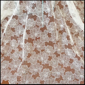 May include: White lace fabric with a floral pattern. The lace has a delicate, intricate design with small flowers and leaves.
