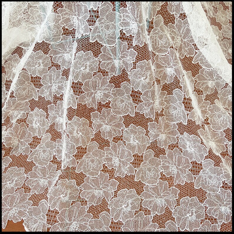 May include: White lace fabric with a floral pattern. The lace has a delicate, intricate design with small flowers and leaves.