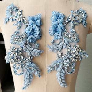 Puede incluir: Dos apliques de encaje floral azul claro. Cada aplique presenta flores de tela, pedrería plateada y delicados detalles de hojas y vides. Los apliques están diseñados para embellecer y proyectos de manualidades.