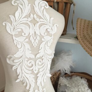 Puede incluir: Aplique de encaje blanco con un dise&ntilde;o floral. El aplique est&aacute; sobre un fondo blanco y tiene un patr&oacute;n delicado e intrincado.