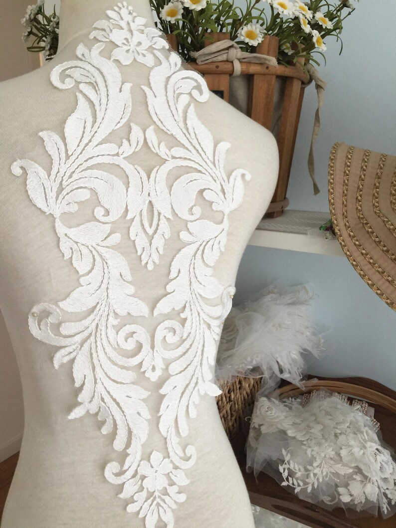Puede incluir: Aplique de encaje blanco con un dise&ntilde;o floral. El aplique est&aacute; sobre un fondo blanco y tiene un patr&oacute;n delicado e intrincado.