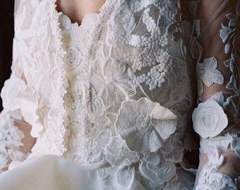 May include: A white lace wedding dress with a high neckline and long sleeves. The dress features intricate floral embroidery and a flowing skirt.