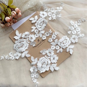 May include: Three white lace appliques with floral designs, featuring delicate flowers and leaves. The appliques are arranged on a brown paper background with the text "Natural Sky" and "Design by Kenzoo".